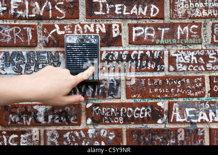 Womans spingendo a mano il vecchio pulsante interfono su muro coperto di graffiti al di fuori di Graceland Memphis, Tennessee, Stati Uniti d'America Foto Stock