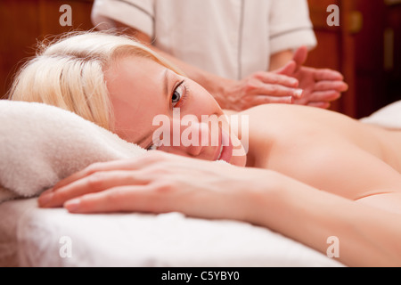 Una donna bionda guardando la telecamera, ricevendo una percussione massaggio schiena in una spa Foto Stock