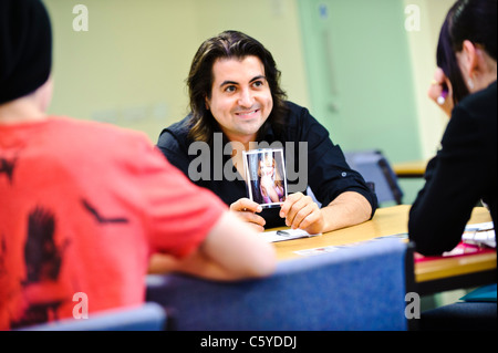 Maschio adulto insegnante in aula con in mano una foto di una celebrità verso la scuola due bambini di età compresa tra 12 a 13 anni Foto Stock