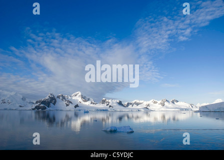 Il profondo blu del cielo con le montagne innevate e iceberg in primo piano con acque calme. Prese a Paradise Harbour, l'Antartide. Foto Stock