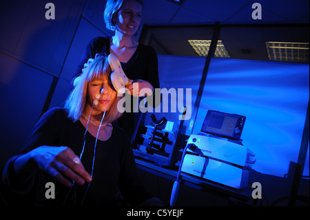 Neurologo usando il tasto pala sagomata per eseguire Transcranial Magnetic stimolazione TMS sul soggetto seduta nel laboratorio luce blu fissa Foto Stock