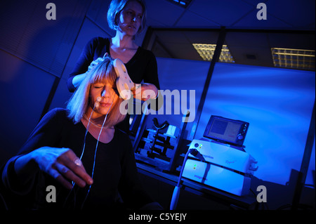 Neurologo usando il tasto pala sagomata per eseguire Transcranial Magnetic stimolazione TMS sul soggetto seduta nel laboratorio luce blu fissa Foto Stock