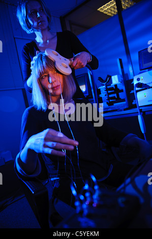 Neurologo usando il tasto pala sagomata per eseguire Transcranial Magnetic stimolazione TMS sul soggetto seduta nel laboratorio luce blu fissa Foto Stock