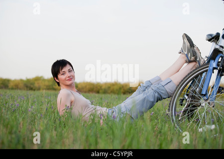 Russia, Voronezh, donna seduta in prato appoggiata sulla bici Foto Stock