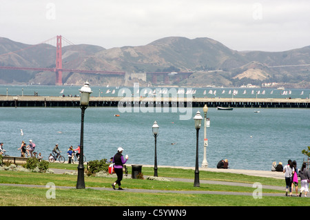 Pedoni godendo di San Francisco Maritime National Historical Park con il Ponte Golden Gate e la baia in background Foto Stock