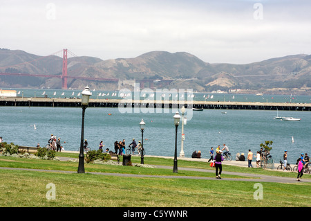 Pedoni godendo di San Francisco Maritime National Historical Park con il Ponte Golden Gate e la baia in background Foto Stock