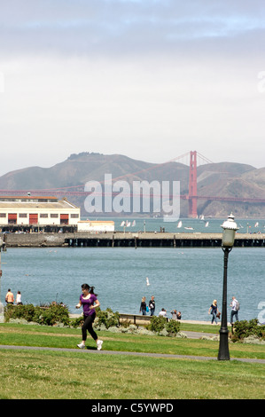 Pedoni godendo di San Francisco Maritime National Historical Park con il Ponte Golden Gate e la baia in background Foto Stock