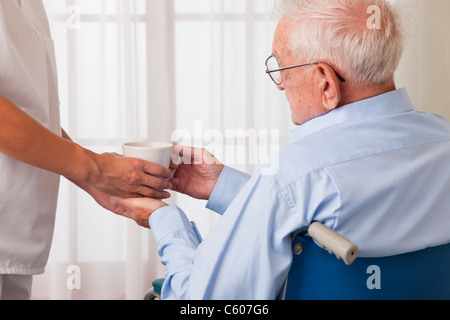 Stati Uniti d'America, Illinois, Metamora, infermiera femmina consegna bevanda senior uomo sulla sedia a rotelle Foto Stock