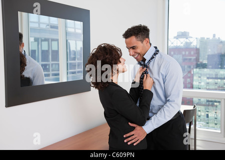 Stati Uniti d'America, New York New York City, giovane donna aiutando uomo sorridente fascetta di legatura nella camera di albergo Foto Stock