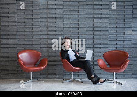 Stati Uniti d'America, New York New York City, ritratto di sorridere giovane donna utilizzando computer portatile nella hall hotel Foto Stock