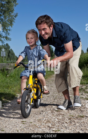 Padre aiutando la figlia in bicicletta Foto Stock