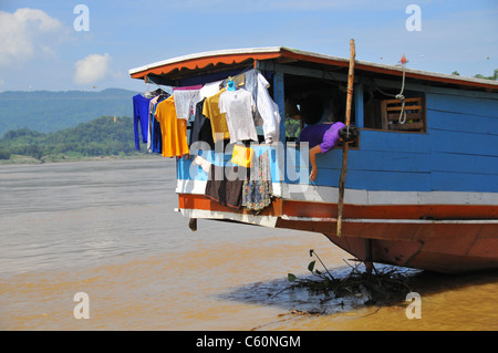 Una donna in una barca fluviale sul fiume Mekong in Laos ASIA, con servizio lavanderia sul retro Foto Stock