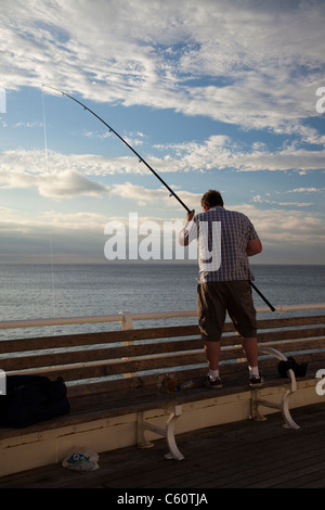 Uomo in piedi su un banco di lavoro mentre la pesca al largo Cromer Pier in Norfolk East Anglia England Foto Stock