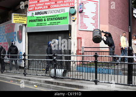 Gioventù mascherato gettando uno scomparto alla polizia di tumulti di strada a Hackney, Londra Foto Stock
