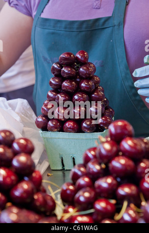 Una donna pilling fresche succose ciliegie in un attraente piramide in vendita in un mercato pubblico Foto Stock