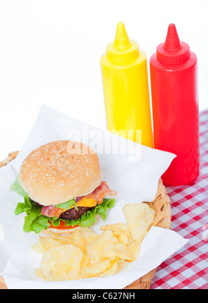 Bacon Cheeseburger e patatine in un cesto con una tovaglia a scacchi e ketchup e senape bottiglie Foto Stock