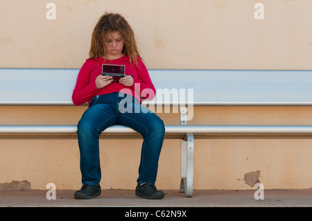 Ragazza adolescente che gioca al vecchio gioco digitale Nintendo sulla panchina Foto Stock