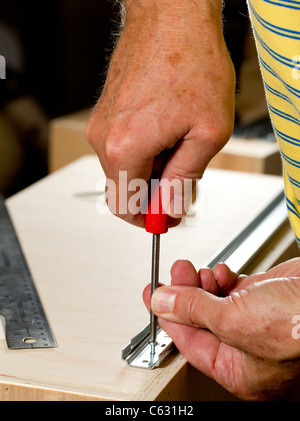 Avvitare una vite in un cassetto guida sul lato del cassetto in legno Foto Stock