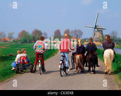 Equitazione per bambini di carretti e pony e biciclette sul rurale elevata canal road in Olanda ultimi mulini a vento e fattorie Foto Stock