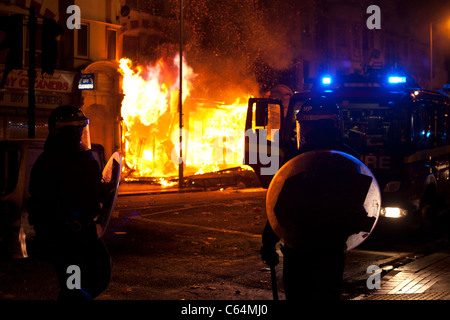 Gli ufficiali di polizia e vigili del fuoco a stare di fronte ad un ardente edificio che sta crollando in Croydon durante l'ago 11 tumulti. Foto Stock