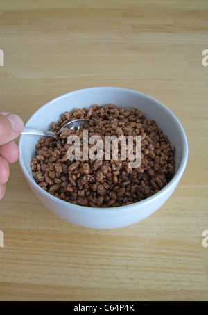 Caucasian adulto maschio utilizzando un cucchiaio per mangiare una ciotola di coco pops cereali per la colazione modello rilasciato Foto Stock