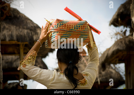 Vista posteriore di una donna balinese che porta offerte religiose in un tradizionale cestino in un tempio indù sulla sua testa Foto Stock