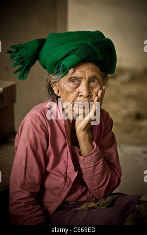 Vecchia donna balinese che indossa una sciarpa verde intorno alla testa, seduta fuori da una baracca Foto Stock