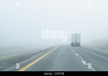 Semi-carrello aziona in caso di nebbia fitta lungo un interstate in montagna. Nebbia fitta crea una strada pericolosa pericolo per qualsiasi driver. Foto Stock