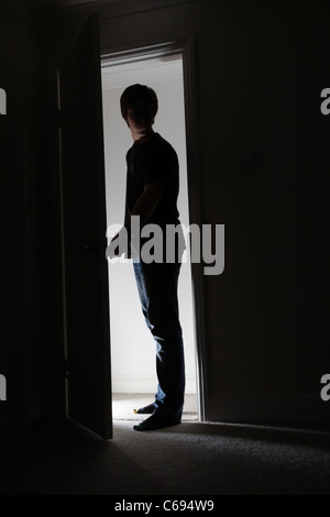 Uomo in piedi in un aprire la porta che conduce a una stanza buia. Foto Stock