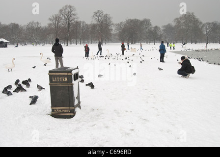 Inferriata accanto allo stagno rotondo in Hyde Park con persone a giocare e alimentando gli uccelli in un giorno di inverni con neve sul terreno Foto Stock