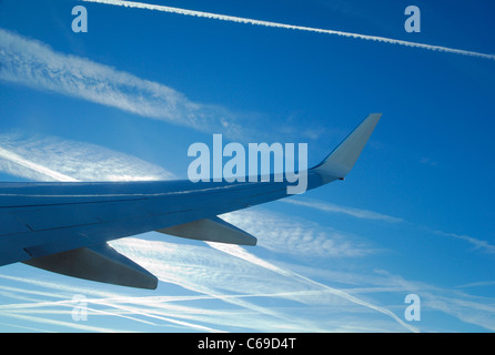 Ala di aereo di linea su un cielo blu pieno di piani di scarico tracce generando cirrus nuvole (Ci) formarsi durante l'inverno, Francia Foto Stock