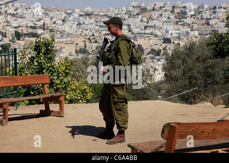 Un soldato israeliano armato è guardia a Tel Rumeida, noto anche come Jabla al-Rahama e citato dai coloni israeliani come Tel Hebron, una località residenziale israeliana che si trova a est di Jebel Rumeida, il più antico sito della città di Hebron Israele in Cisgiordania Foto Stock