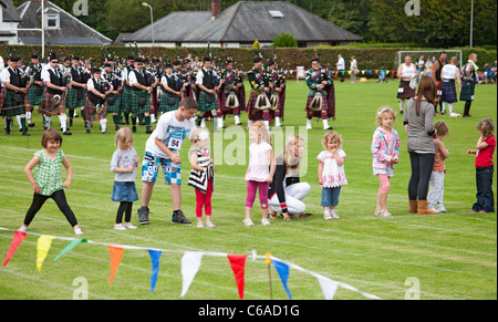 I genitori e le loro figlie: la linea di partenza di una gara per le ragazze piccole a Brodick Giochi delle Highland, Arran. Bande di cornamuse in background. Foto Stock