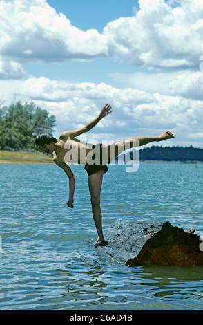 Asian teen saldi sul tronco galleggiante nel lago blu durante la lunga estate calda mentre è in vacanza Foto Stock