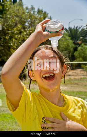 Una ragazza adolescente si versa acqua fredda su se stessa in un pomeriggio caldo in arancione, CA. Foto Stock