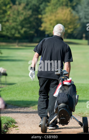 Un golfista tirando il suo carrello con attrezzatura da golf lungo il percorso a Stanmore campo da golf su una soleggiata giornata estiva. Foto Stock