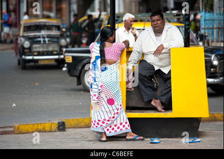 Un sovrappeso Taxi Dispatcher in una conversazione con una donna da un Mumbai Taxi Stand vicino al Gateway di India. Foto Stock