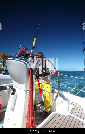 Uomo al timone di una barca a vela in blue sky meteo Foto Stock
