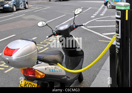 Auto elettrica della stazione di ricarica e ricarica della baia di parcheggio occupato da scooter batteria collegata al pilastro di energia elettrica del cavo giallo street scene London REGNO UNITO Foto Stock