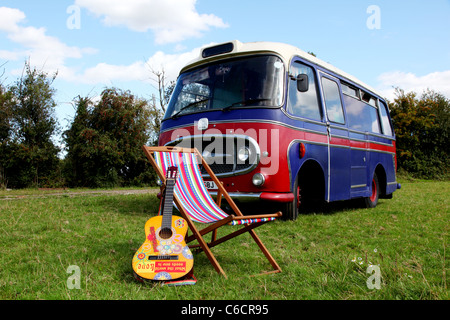 1971 Bedford camper parcheggiato in un campo con una chitarra acustica e una sedia a sdraio in primo piano. Foto Stock