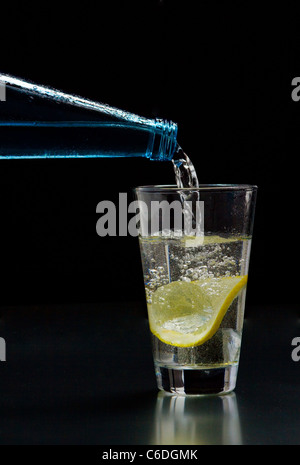 L'acqua minerale è versata in un bicchiere con ghiaccio e limone Foto Stock