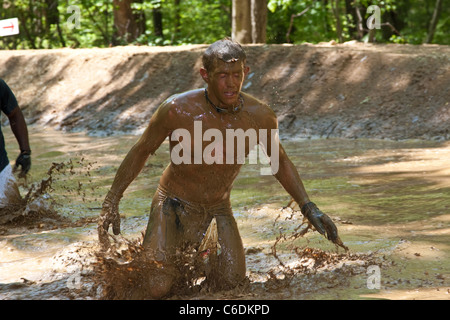 Un robusto Mudder partecipante corre attraverso il 'Swamp Stomp'' sezione del corso. Mudder resistente è una giornata di sport estremi Foto Stock