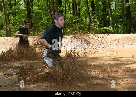 Un robusto Mudder partecipante corre attraverso il 'Swamp Stomp'' sezione del corso. Mudder resistente è una giornata di sport estremi Foto Stock