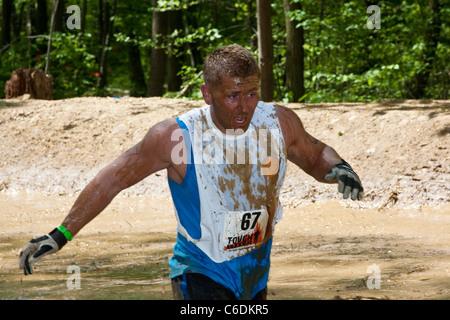 Un robusto Mudder partecipante corre attraverso il 'Swamp Stomp'' sezione del corso. Mudder resistente è una giornata di sport estremi Foto Stock