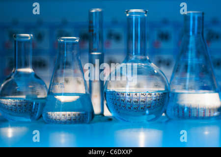 Becher e matracci con tabelle periodiche in laboratorio Foto Stock