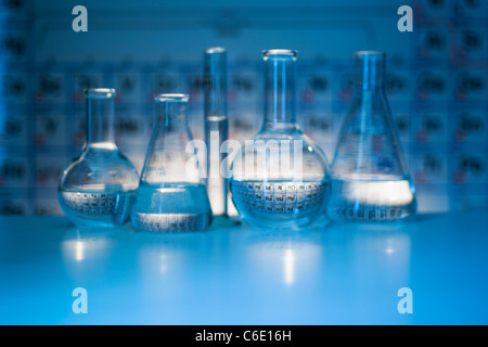 Becher e matracci con tabelle periodiche in laboratorio Foto Stock