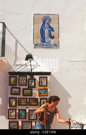 Donna che spazzava di fronte a un negozio di souvenir che vende dipinti. Torremolinos, Provincia di Malaga, Costa del Sol, Spagna. Foto Stock