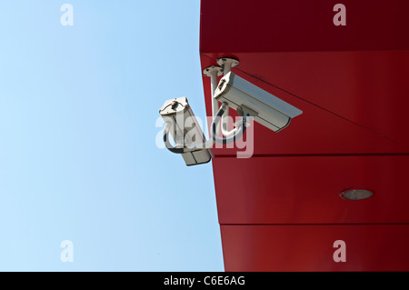 Due videocamere di sorveglianza sul cielo blu e rosso sfondo a parete Foto Stock