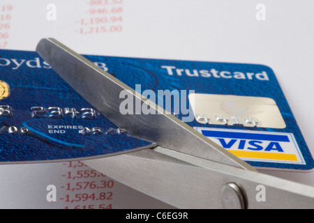 Un paio di forbici il taglio di una carta di credito Visa in stretta fino al di sopra di un foglio di conti che mostra i debiti in rosso. Inghilterra, Regno Unito, Gran Bretagna Foto Stock