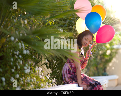 Stati Uniti d'America, Arizona, Scottsdale, giovane donna sorridente seduto sul muro e palloncini di contenimento Foto Stock